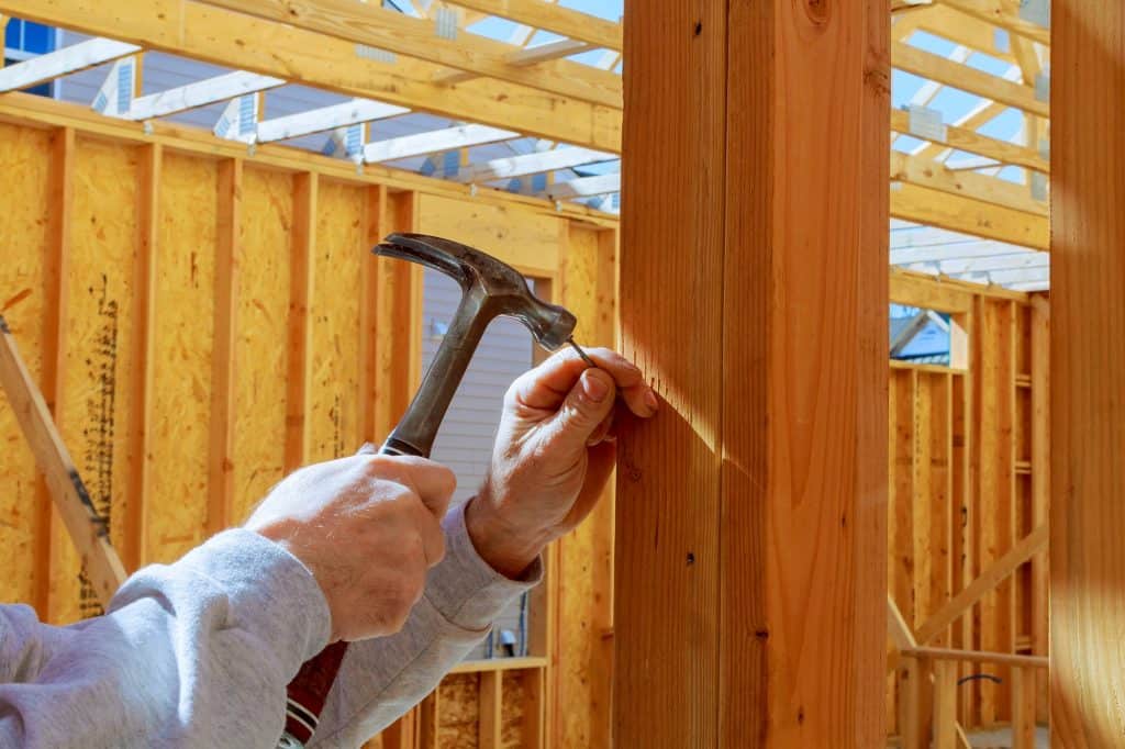 builder hammers a nail into a wooden beam New building home, nailing hammer