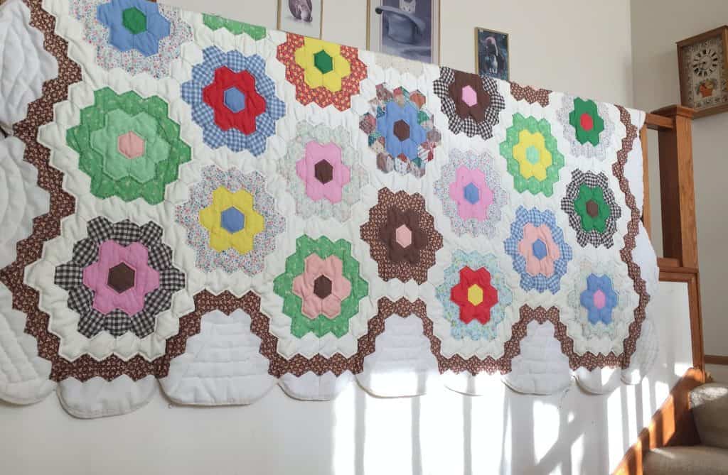 Grandmother’s Flower Garden pattern on handmade quilt hanging over banister