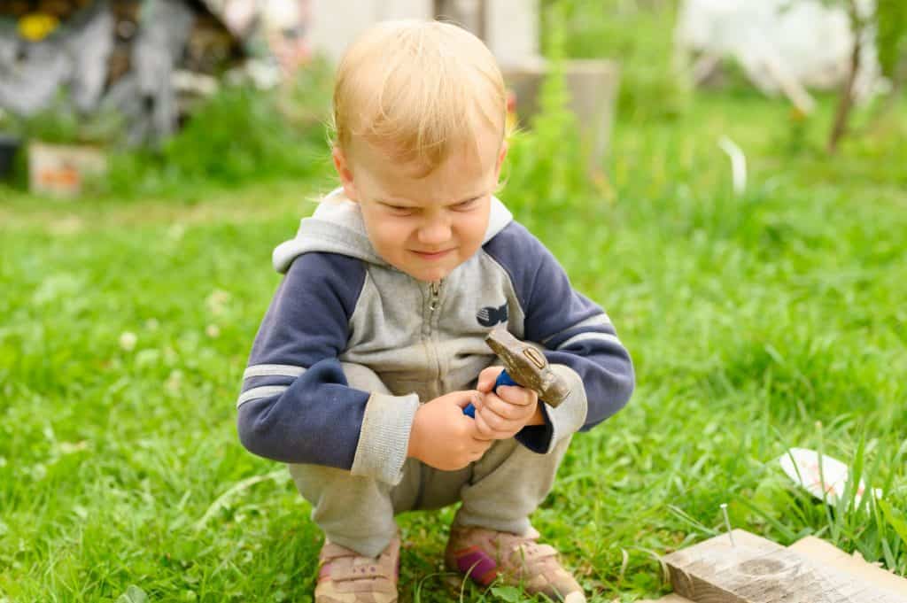 little angry boy hammering a nail with a hammer in the village