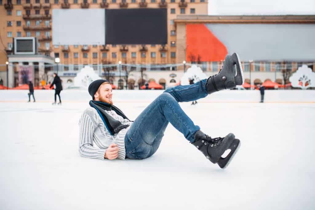 Young man in skates sitting on ice, skating rink