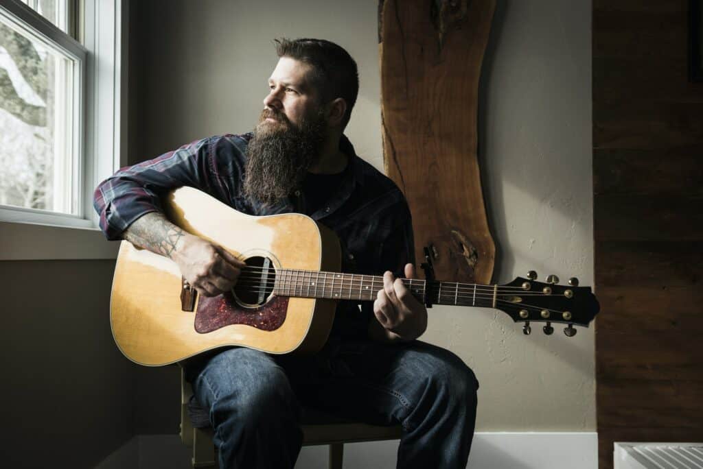 Man playing guitar beside window