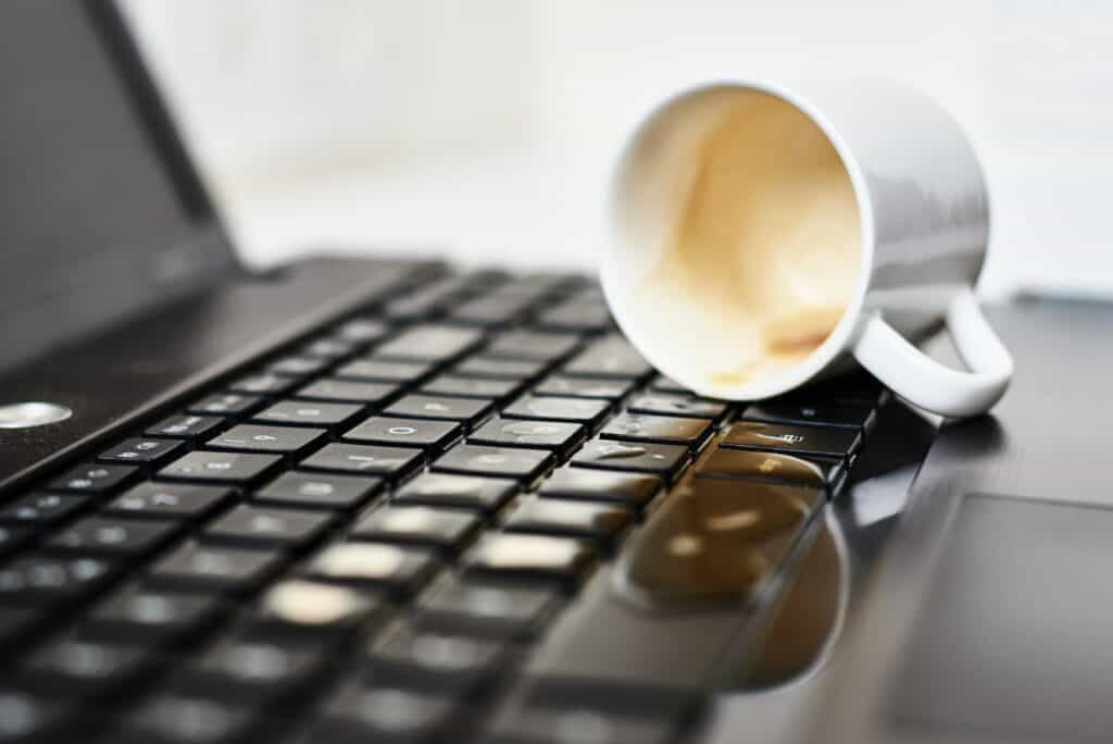 Spill coffee from white cup on the computer laptop keyboard.Damage to computer due to spilled liquid